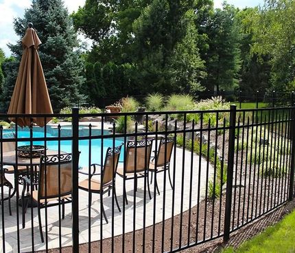 Backyard patio with fenced swimming pool, table and chairs, and a closed umbrella