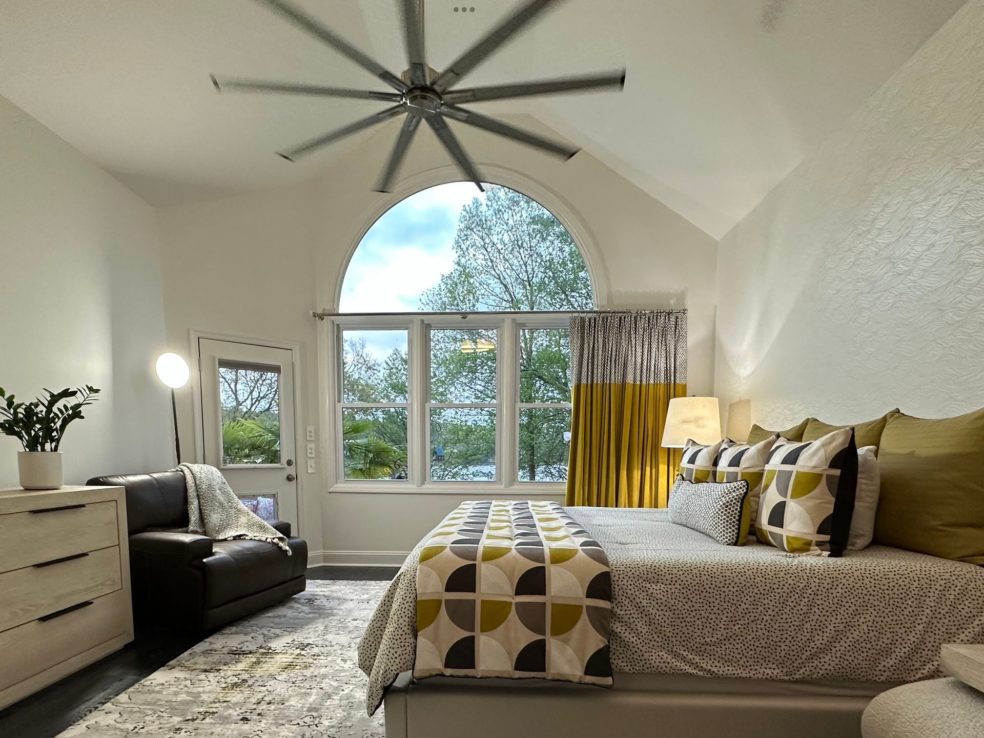 Bedroom with arched window, bed, dark armchair, and patterned curtains.