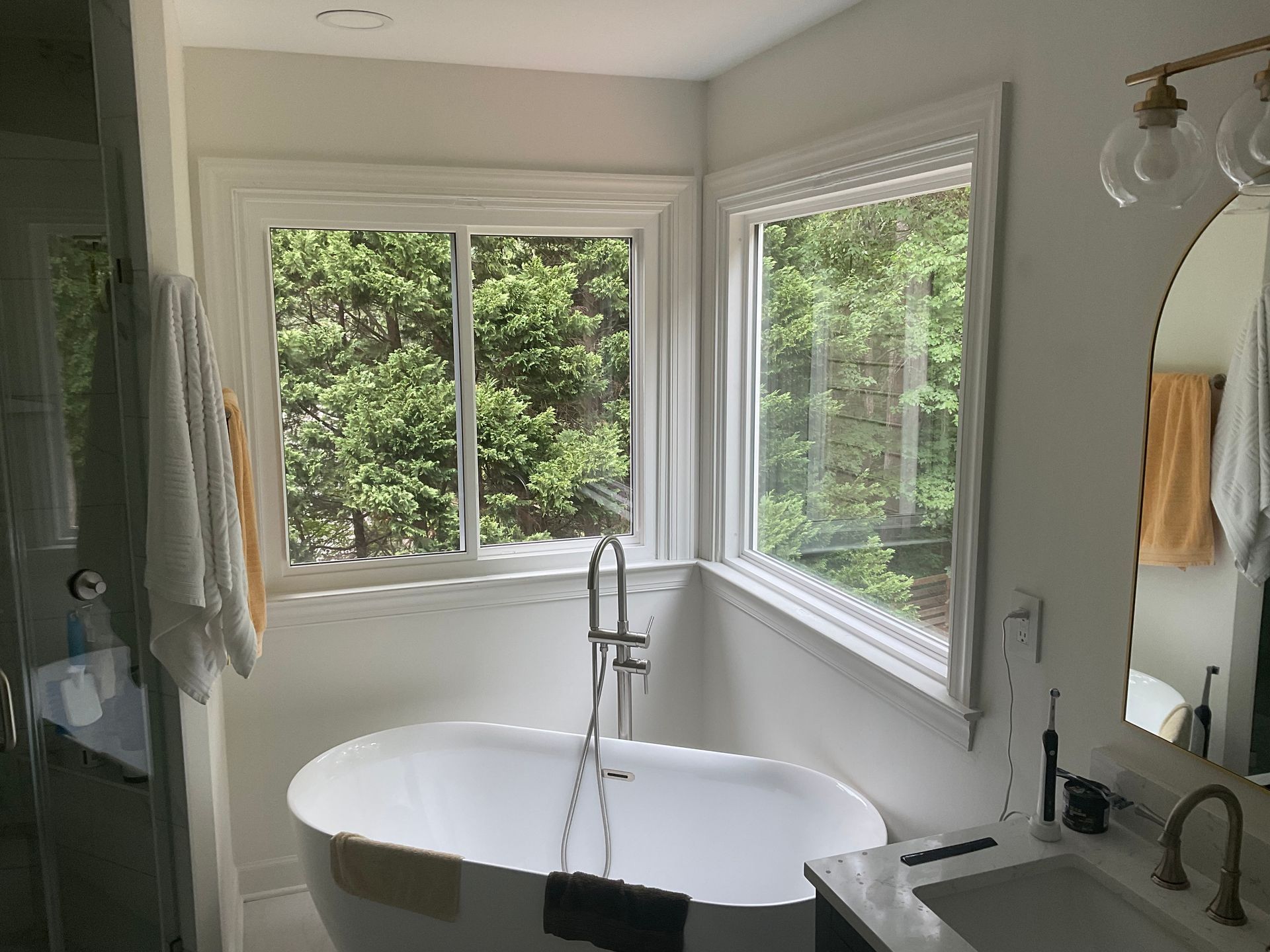 Bathroom with a white soaking tub, two windows with forest view, and white trim.