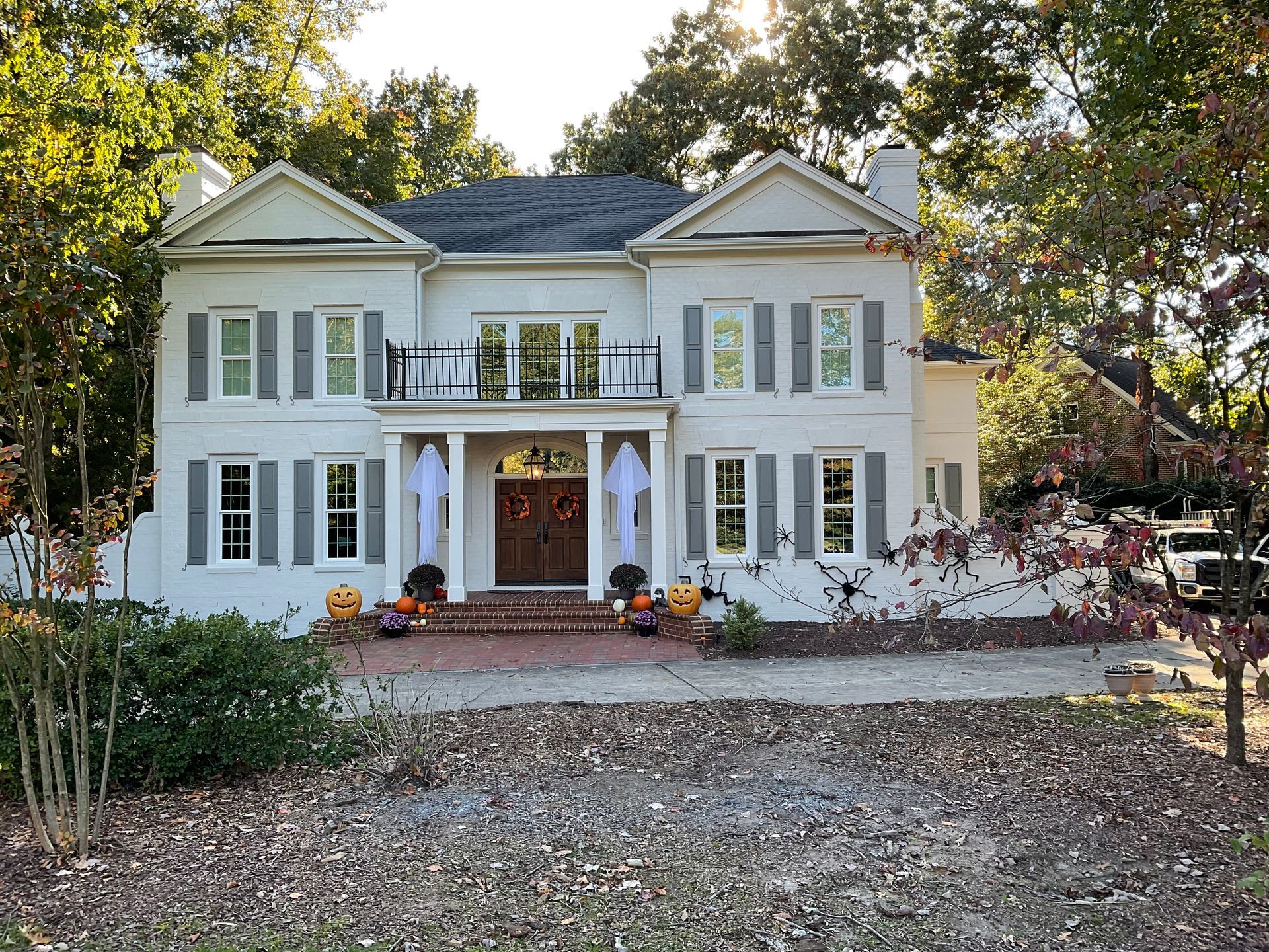 Two-story white house with gray shutters and Halloween decorations, including ghosts and pumpkins.