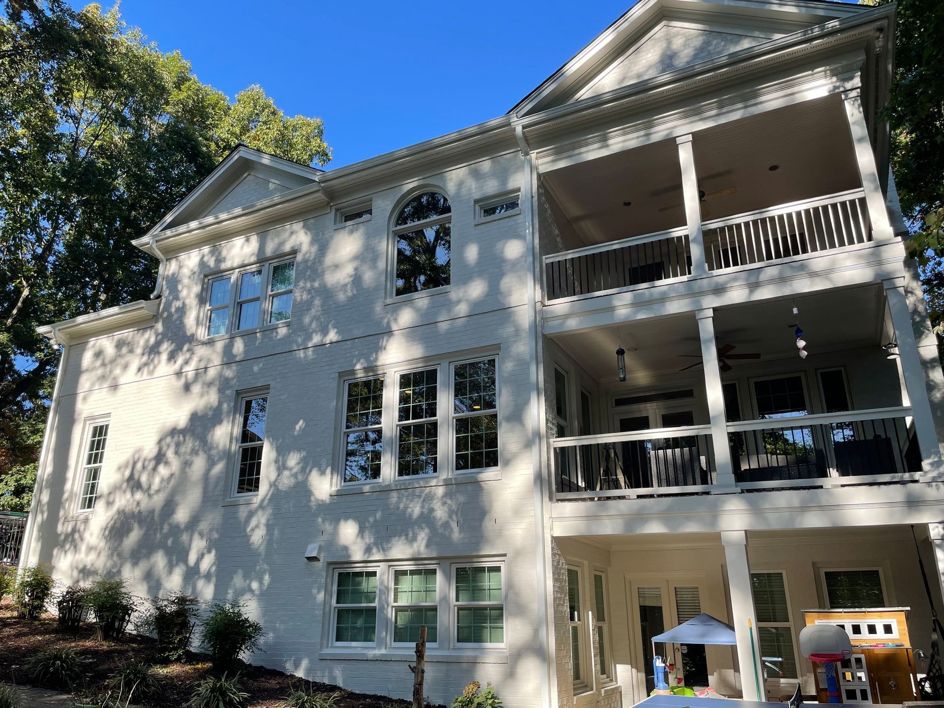 White brick home with two-story balcony, green trees, and blue sky.