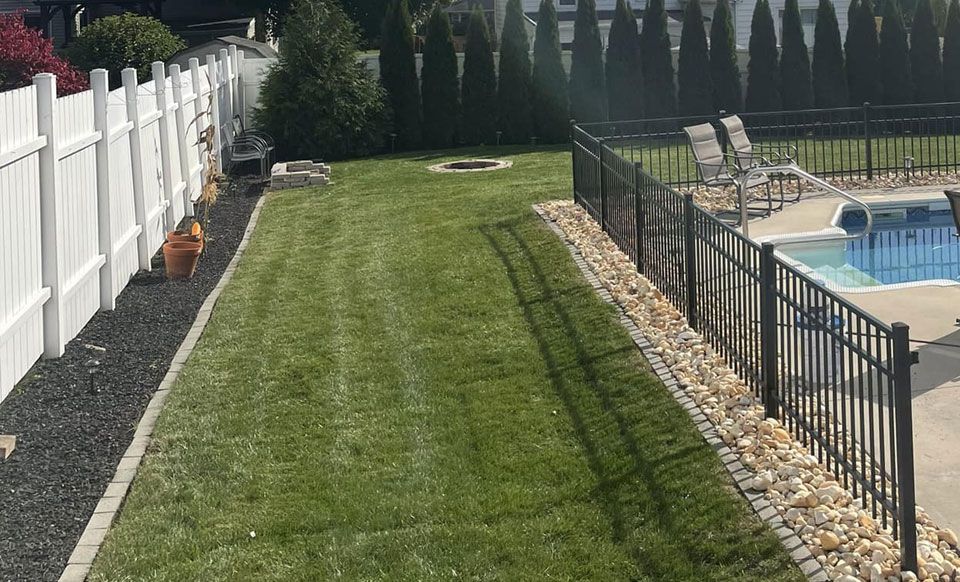 A fence surrounds a lush green lawn next to a pool.