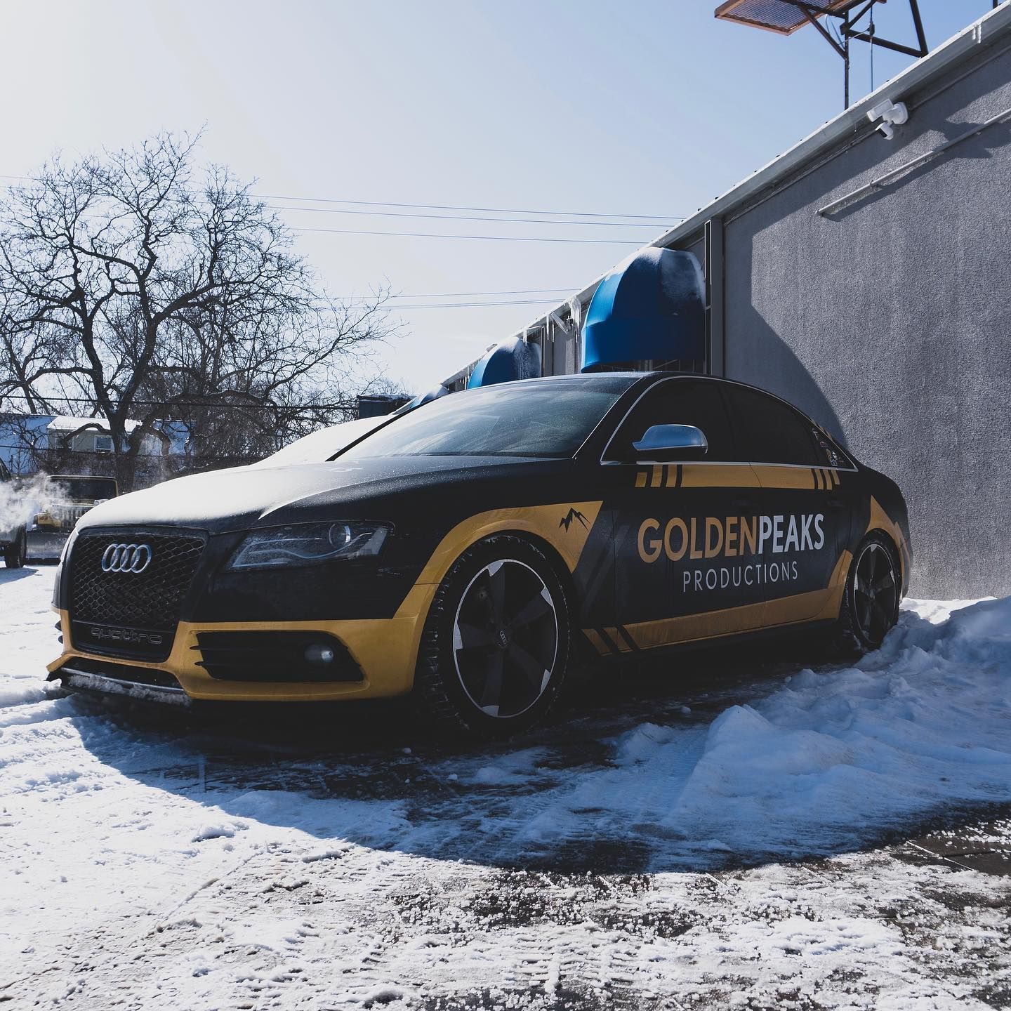 A black and yellow car with the word golden peaks on the side is parked in the snow