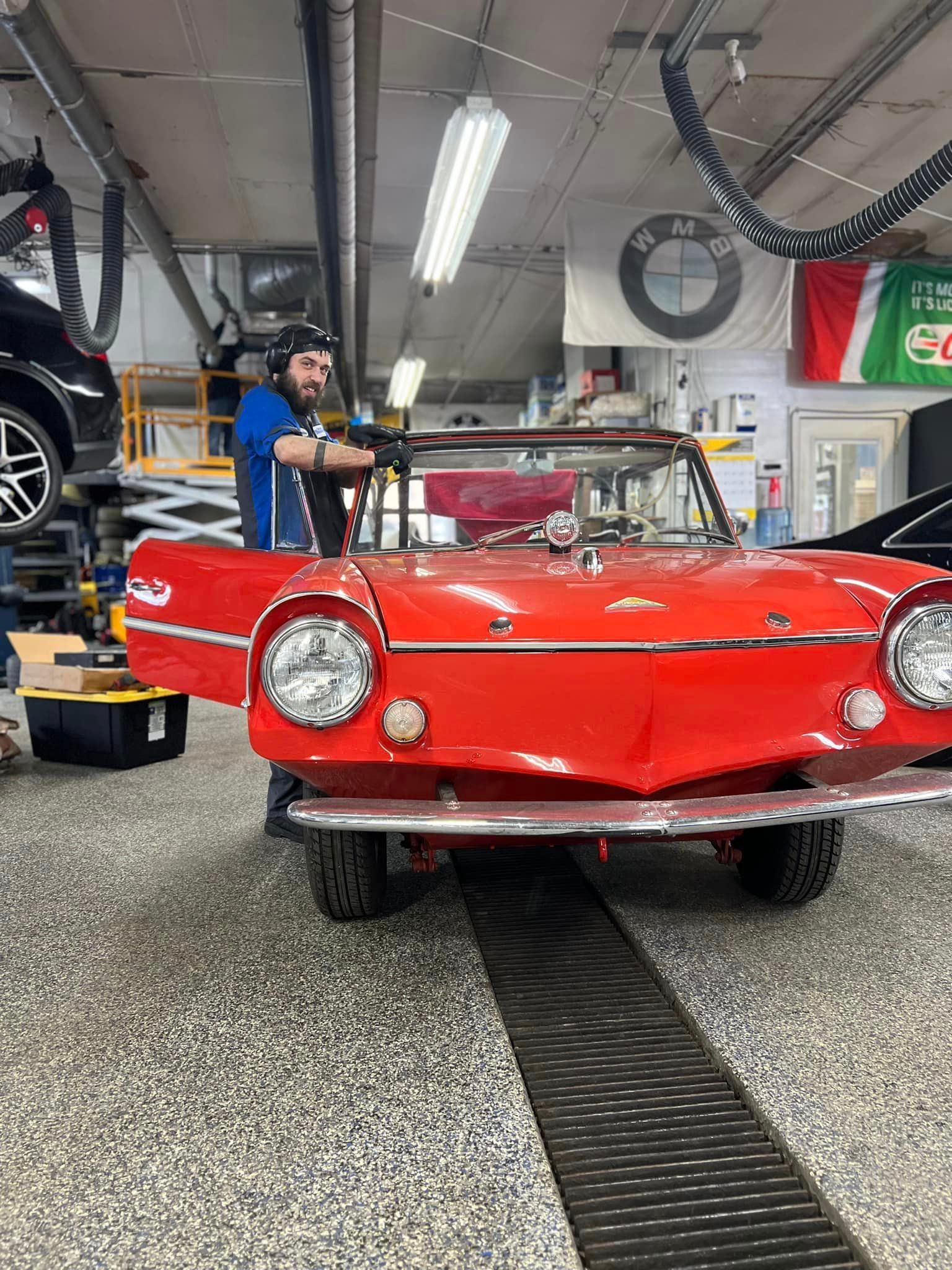 A man is working on a red car in a garage.
