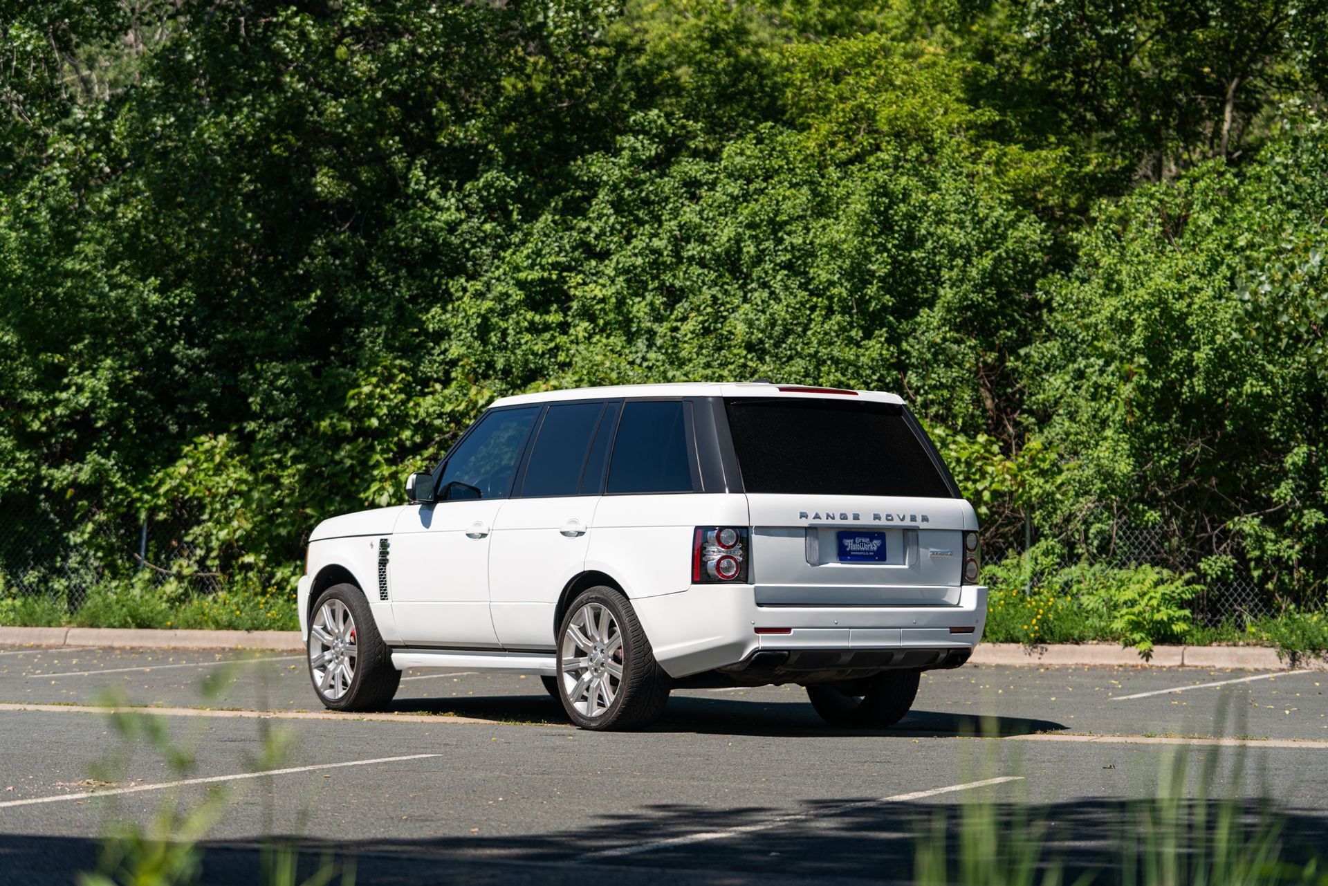A white range rover is driving down a road with trees in the background.