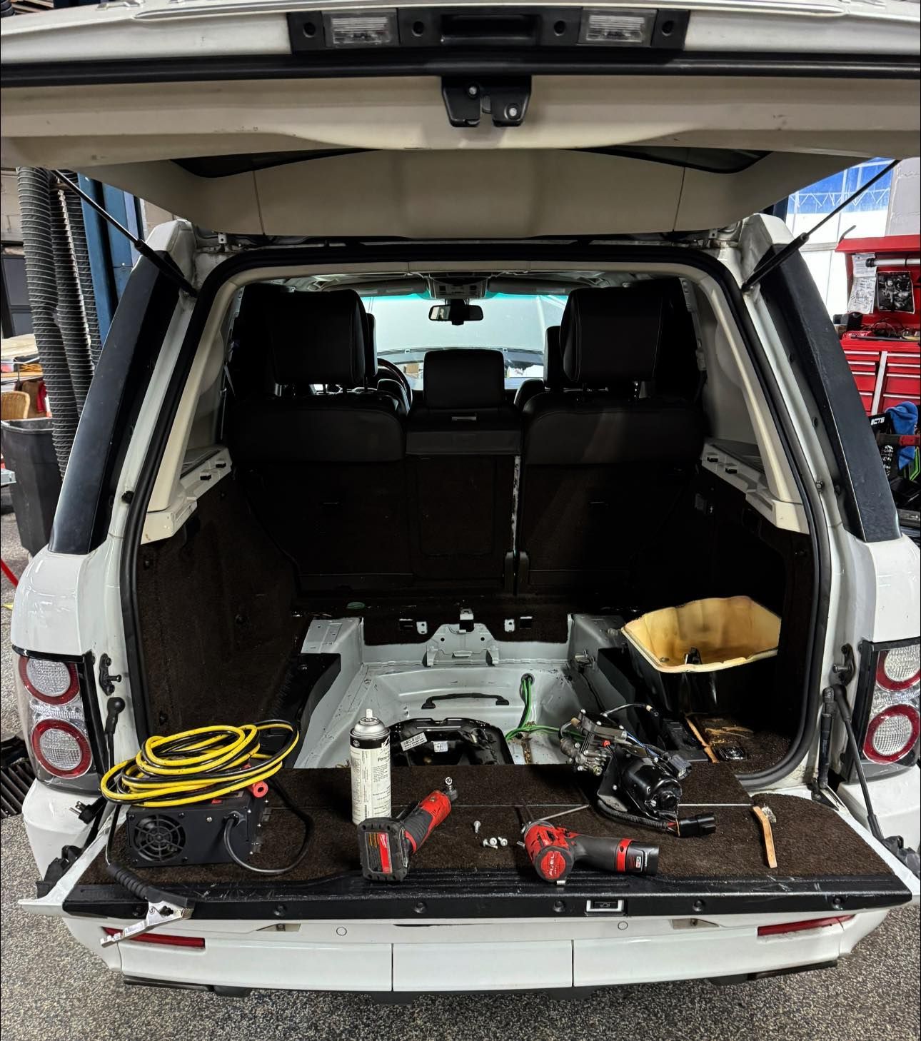 The trunk of a range rover is open and filled with tools.
