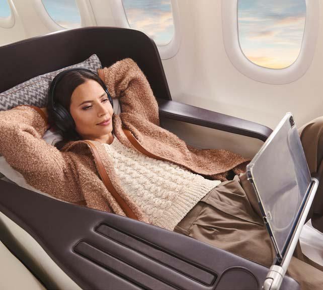 A woman wearing headphones is laying on an airplane using a laptop