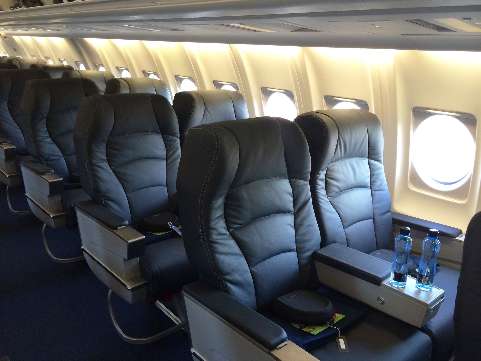 A row of empty seats on an airplane with bottles of water on the arm rests.