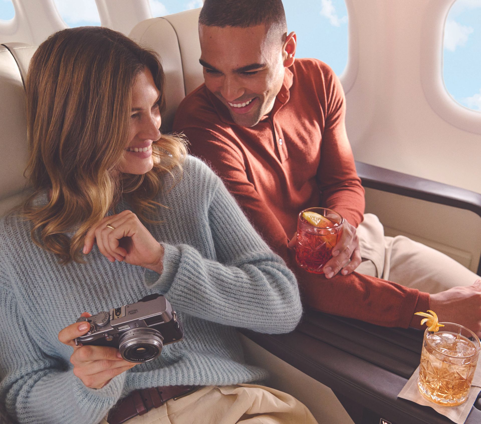 A man and a woman are sitting on an airplane and the woman is holding a camera