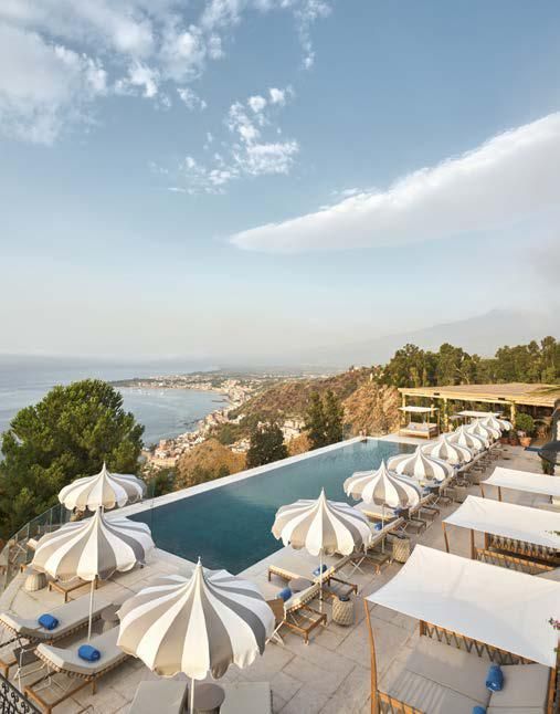 A swimming pool surrounded by umbrellas and chairs with a view of the ocean