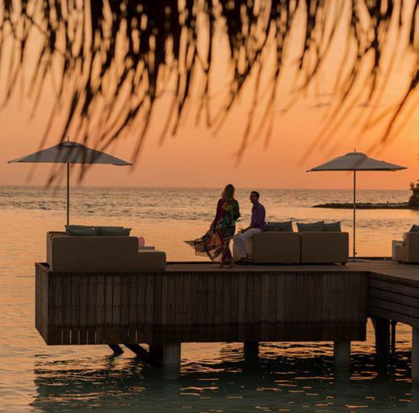 A couple sitting on a dock overlooking the ocean at sunset