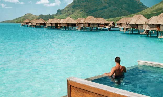 A man is sitting in a swimming pool overlooking the ocean.