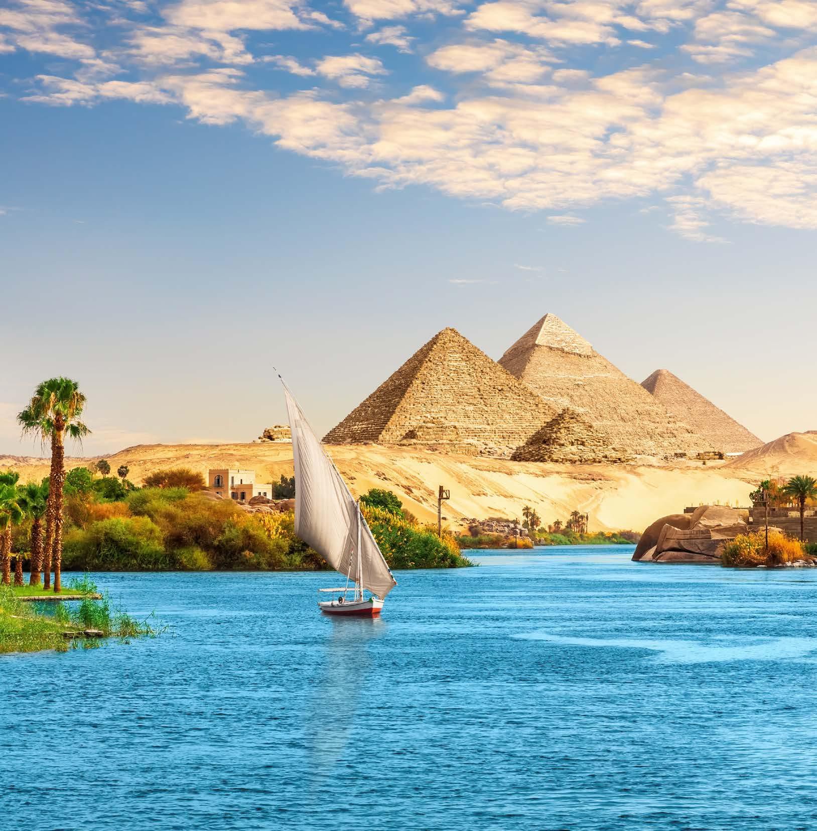 A sailboat is floating on a river with pyramids in the background.