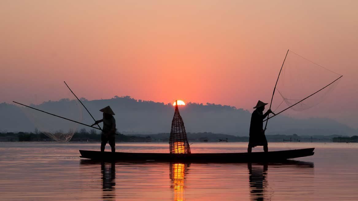 Two people are fishing in a boat on a lake at sunset.