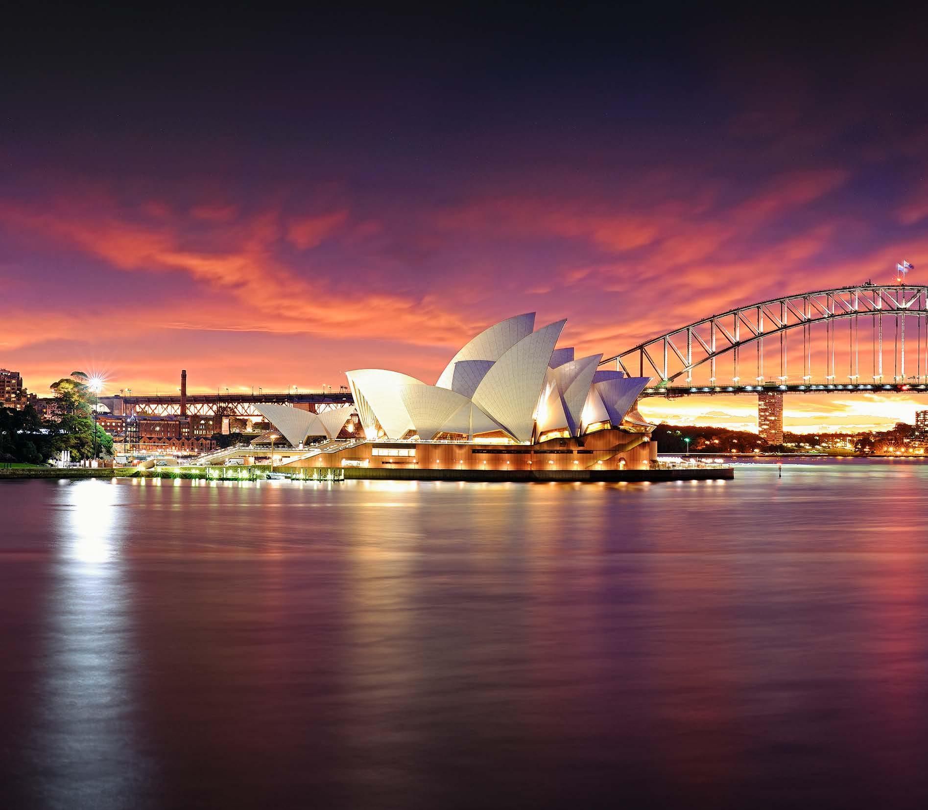 The sydney opera house is lit up at night with a bridge in the background
