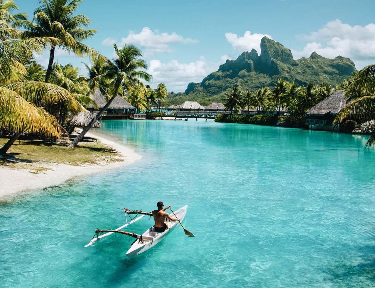 A man is paddling a kayak in the ocean near a beach.