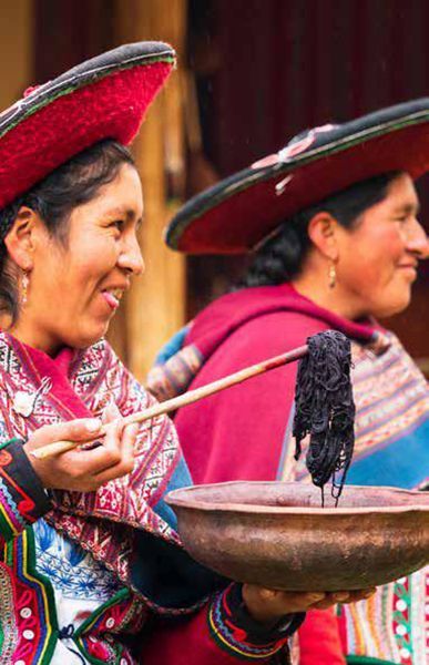 Two women in traditional clothing are holding a bowl of food.