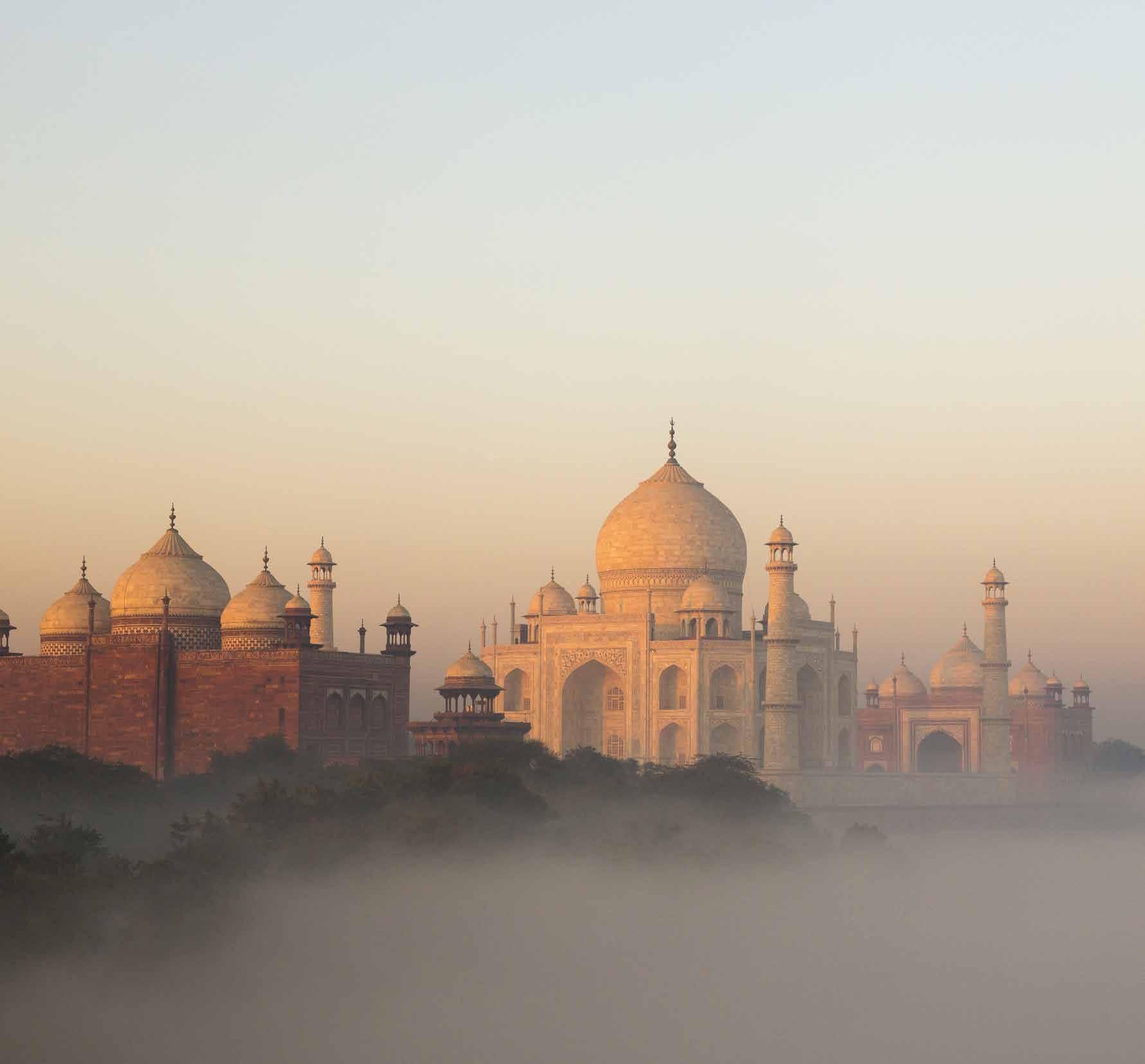The taj mahal is covered in fog at sunrise.