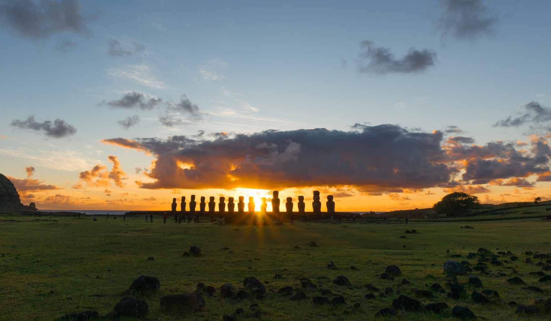 The sun is setting behind a row of statues in a field.
