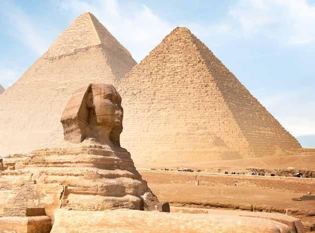 The sphinx is in front of two pyramids in the desert.