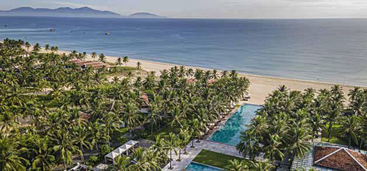 An aerial view of a beach with palm trees and a large swimming pool.