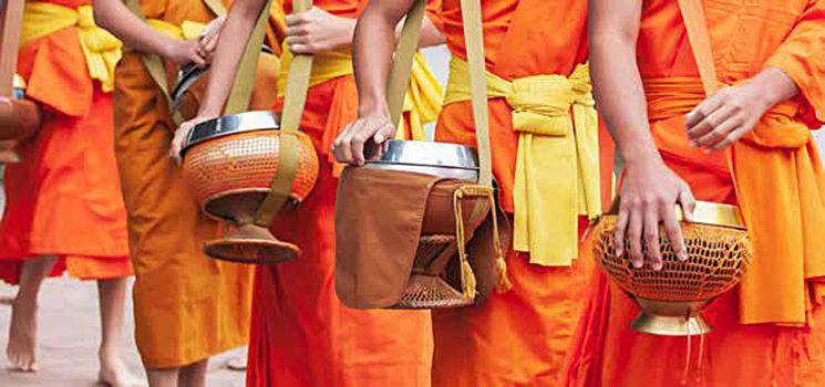 A group of monks in orange robes are walking down a street holding bowls.