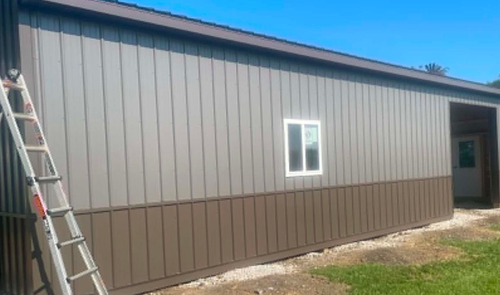 Exterior of a brown metal building with a ladder leaning against the left side and a small window.