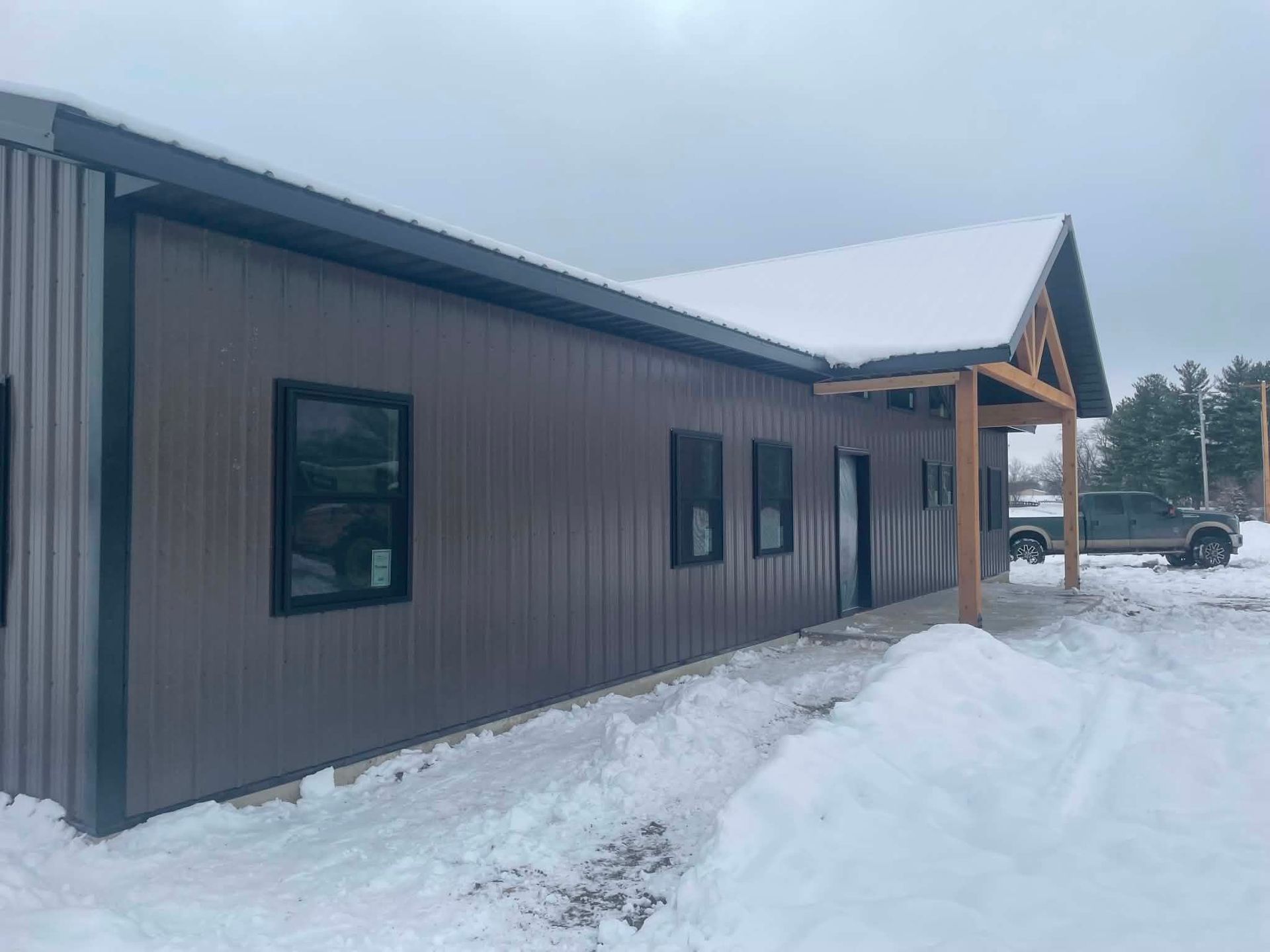 Snowy exterior of a brown building with a covered entrance and windows, surrounded by snowbanks