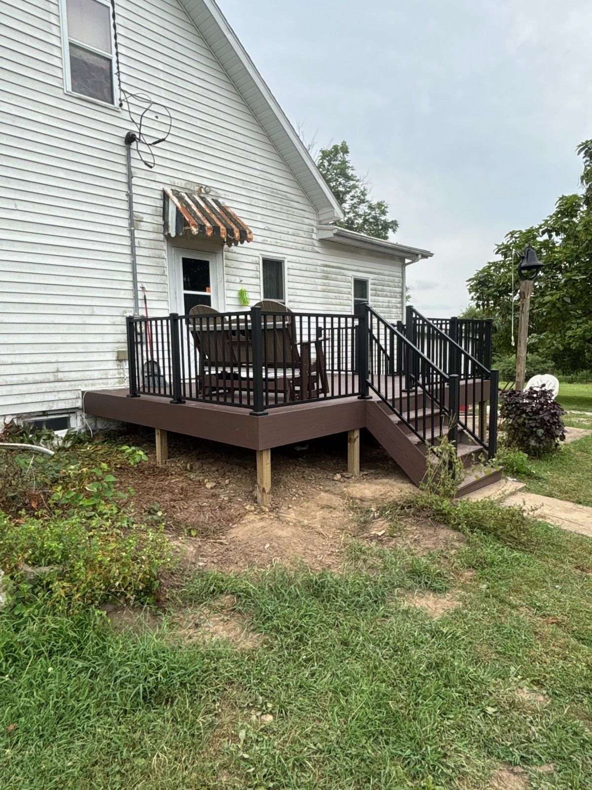 White house with a small brown deck, black railing, and stairs in a grassy yard.