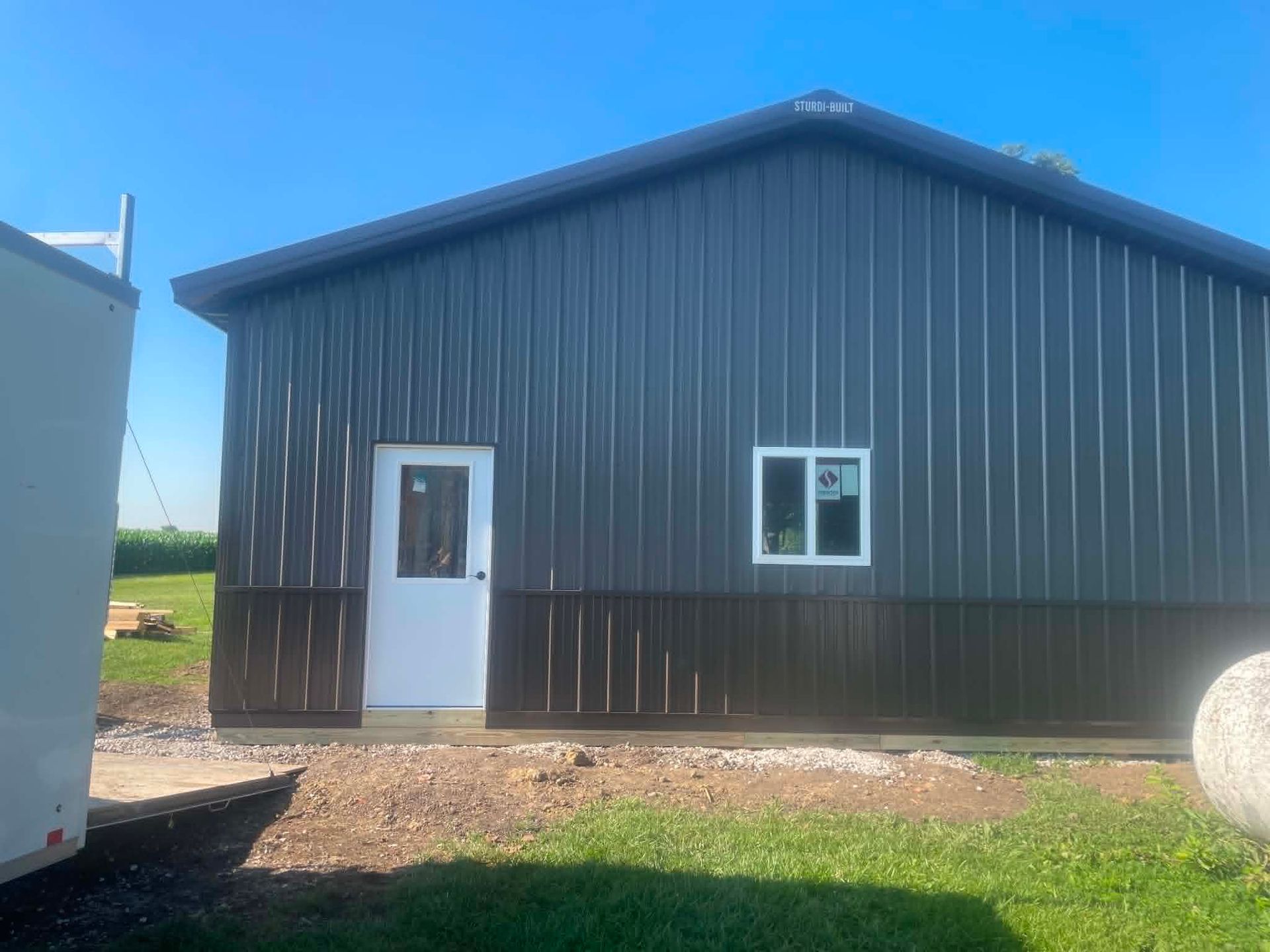 Dark metal building with a white door and window under a blue sky.