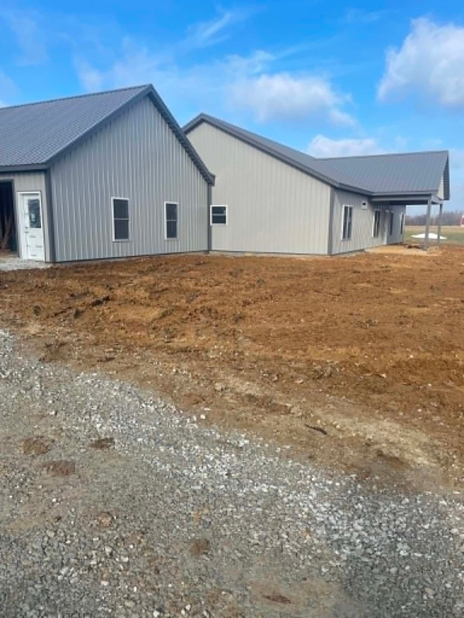 Gray metal-sided house under construction with bare dirt and gravel foreground under a blue sky