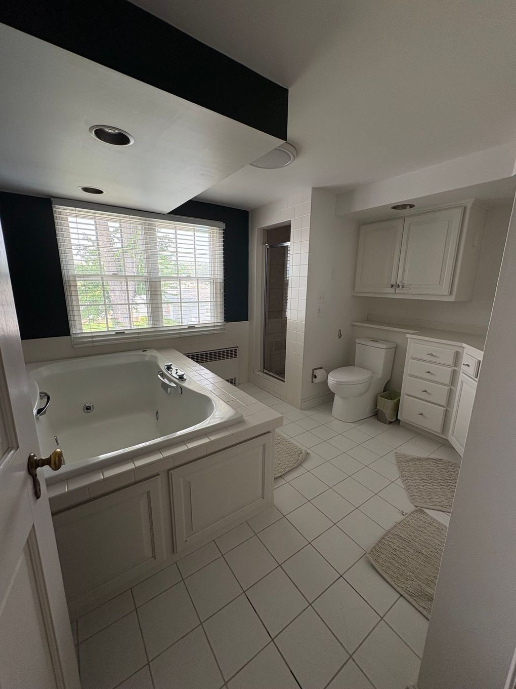 White bathroom with a jacuzzi tub, toilet, cabinets, and shower.