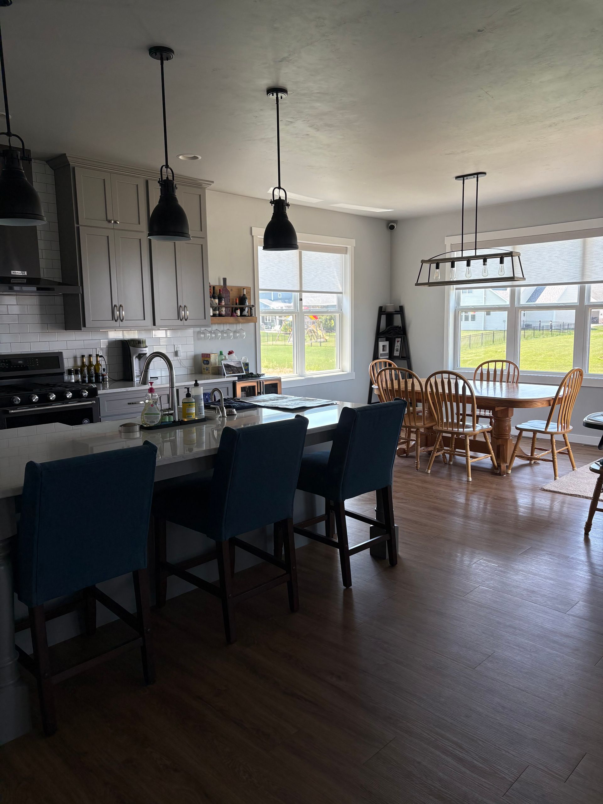 Kitchen with island and seating, a dining table, and dark pendant lights.