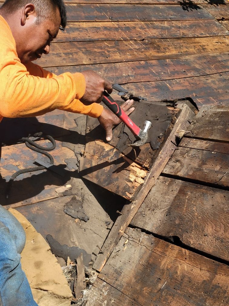 A man wearing a hard hat is working on the roof of a house.