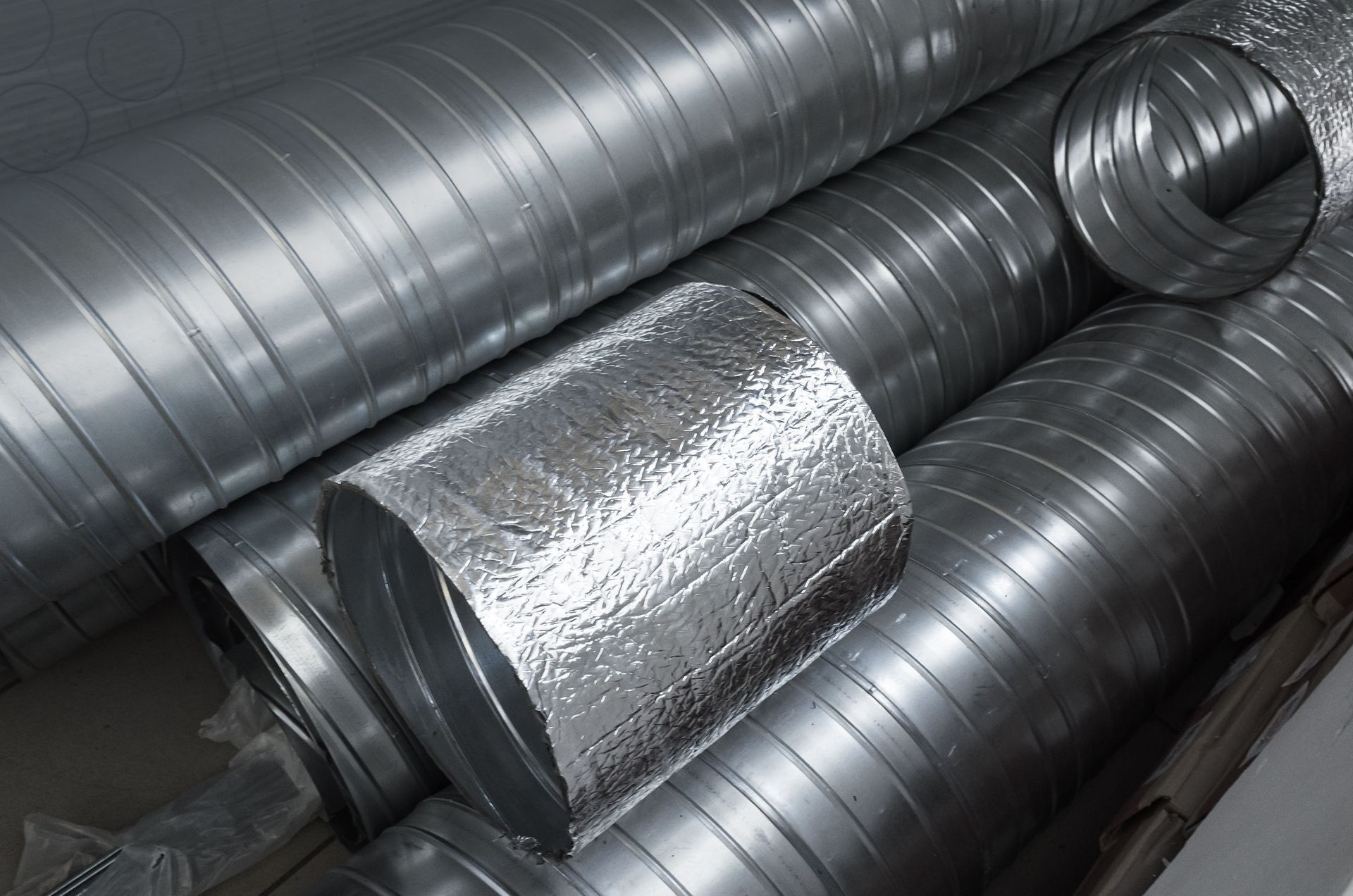 Galvanized metal ductwork, one section insulated with silver foil.