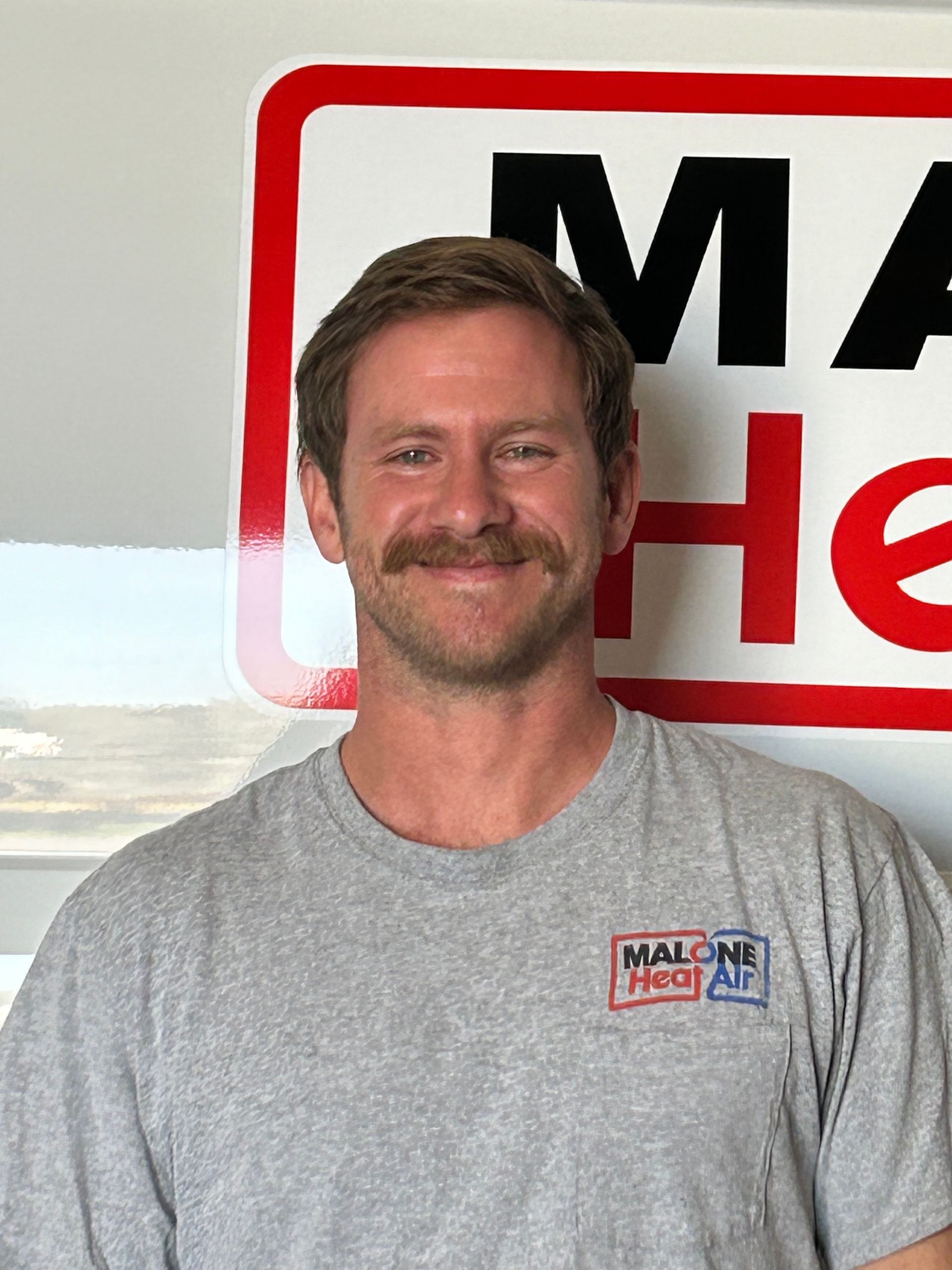 Man with mustache in front of a red and white sign for 