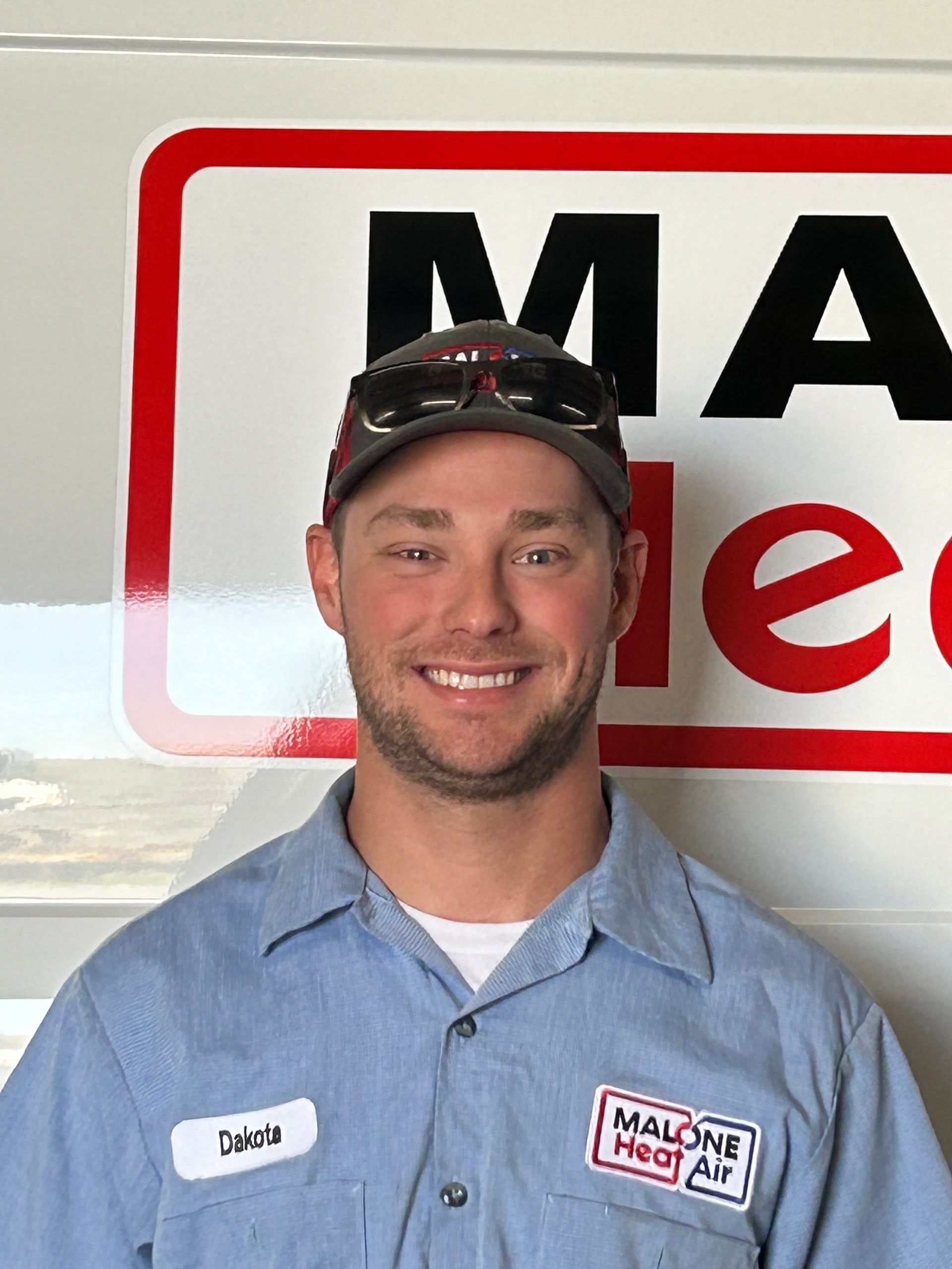 Man in a blue work shirt, smiling, in front of a sign for 