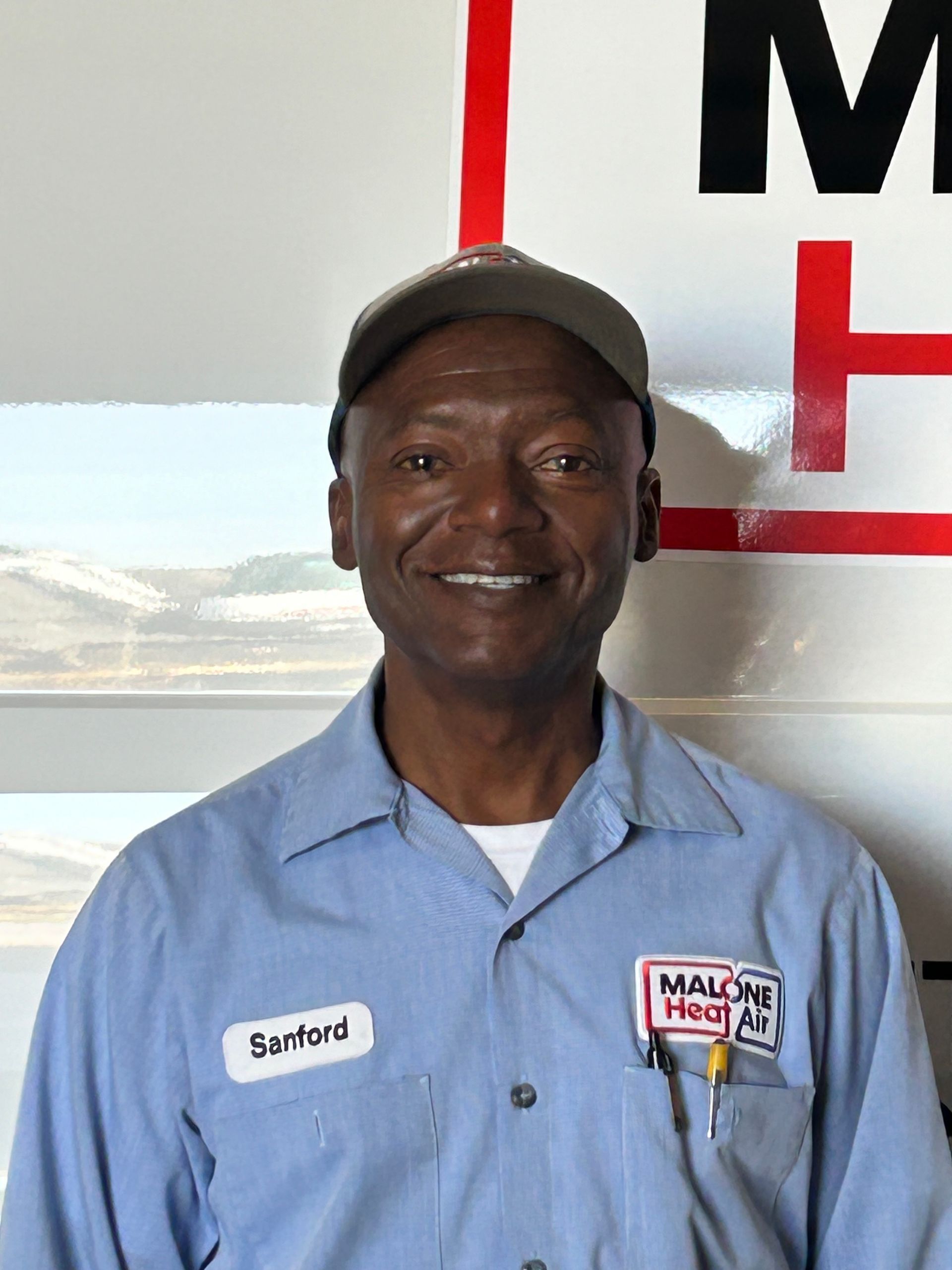 Man wearing a blue work shirt, cap, and name tag that reads 