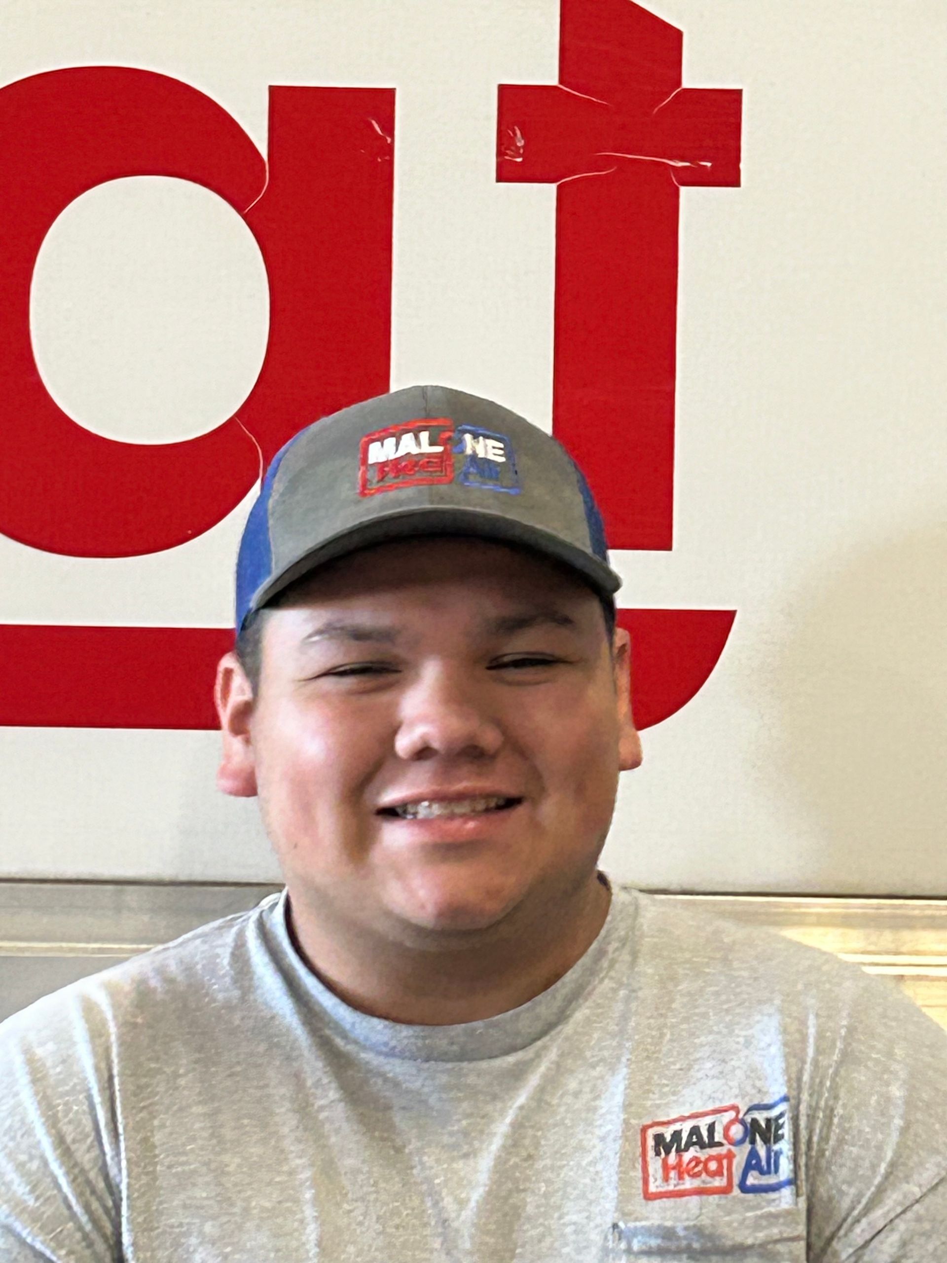 Man wearing hat and t-shirt, smiling in front of a sign.