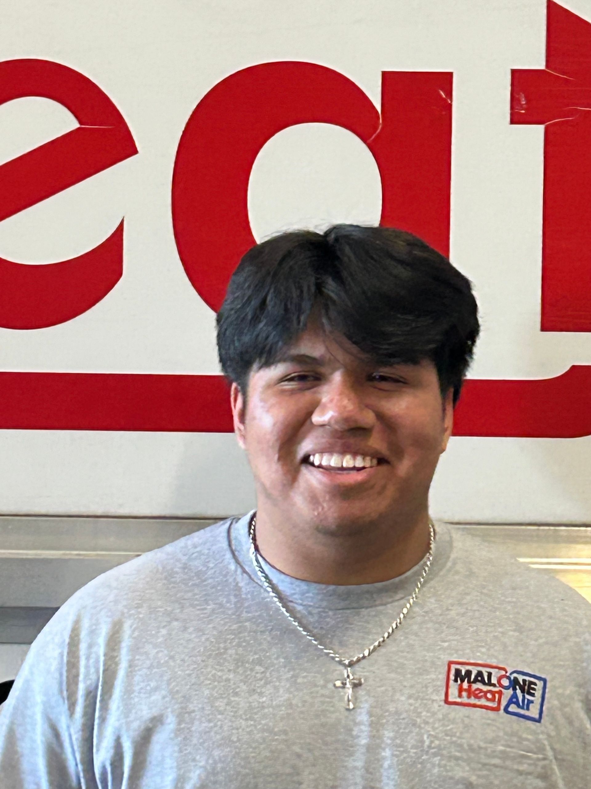 Man smiling in front of a red and white sign with the word 
