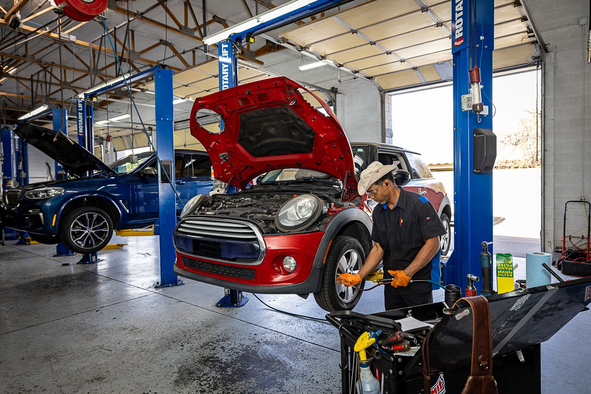 A mechanic works on a red Mini Cooper in a car repair shop.