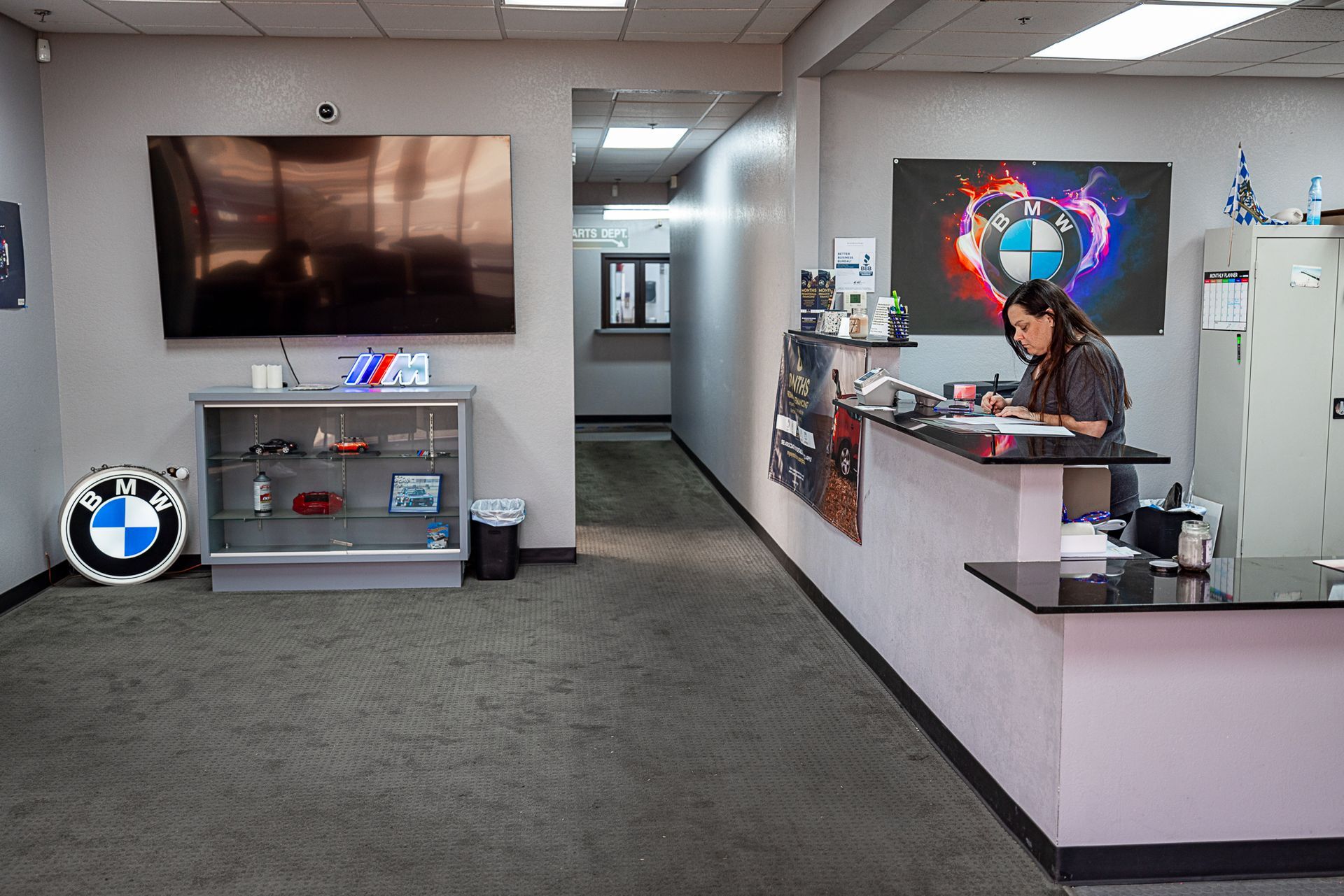 Reception area with woman at desk, BMW logo on wall, TV, display case, and hallway.