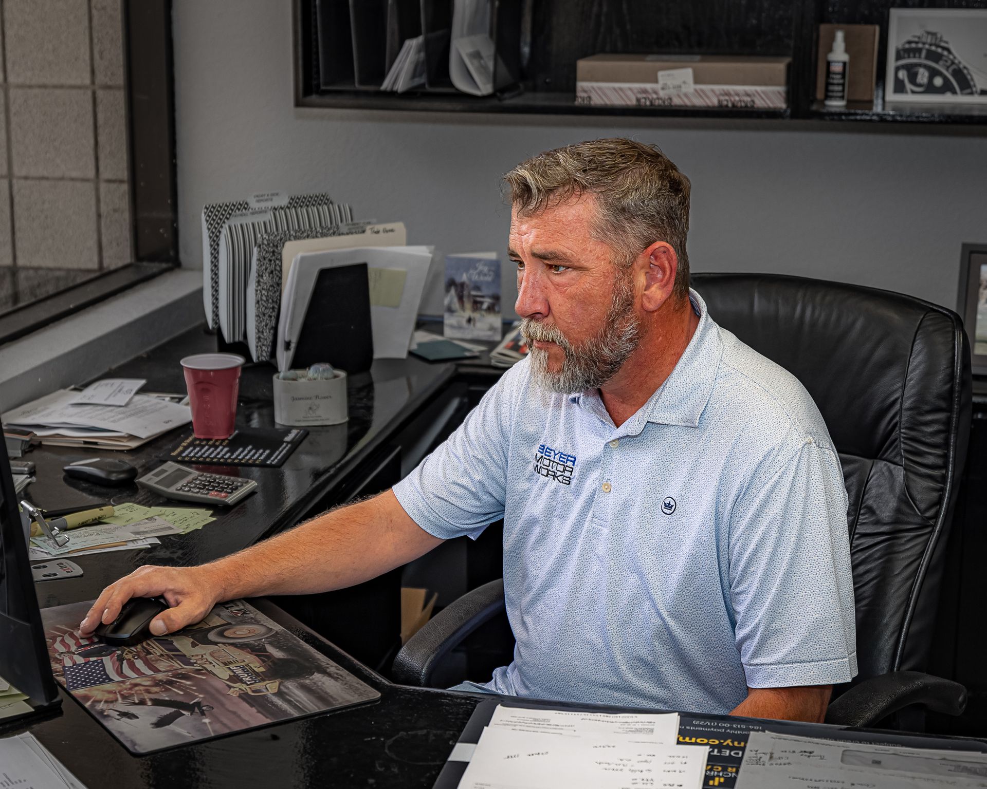 Man at a desk using a computer, wearing a light blue polo shirt, in an office setting.