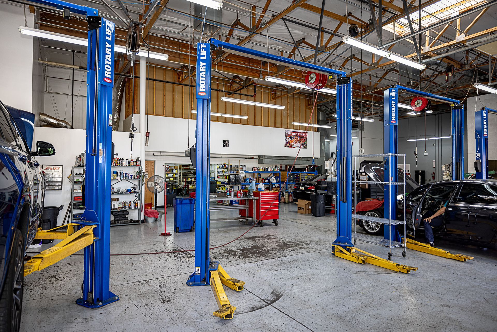 Car repair shop interior with blue lifts and cars, equipment, and a red toolbox.