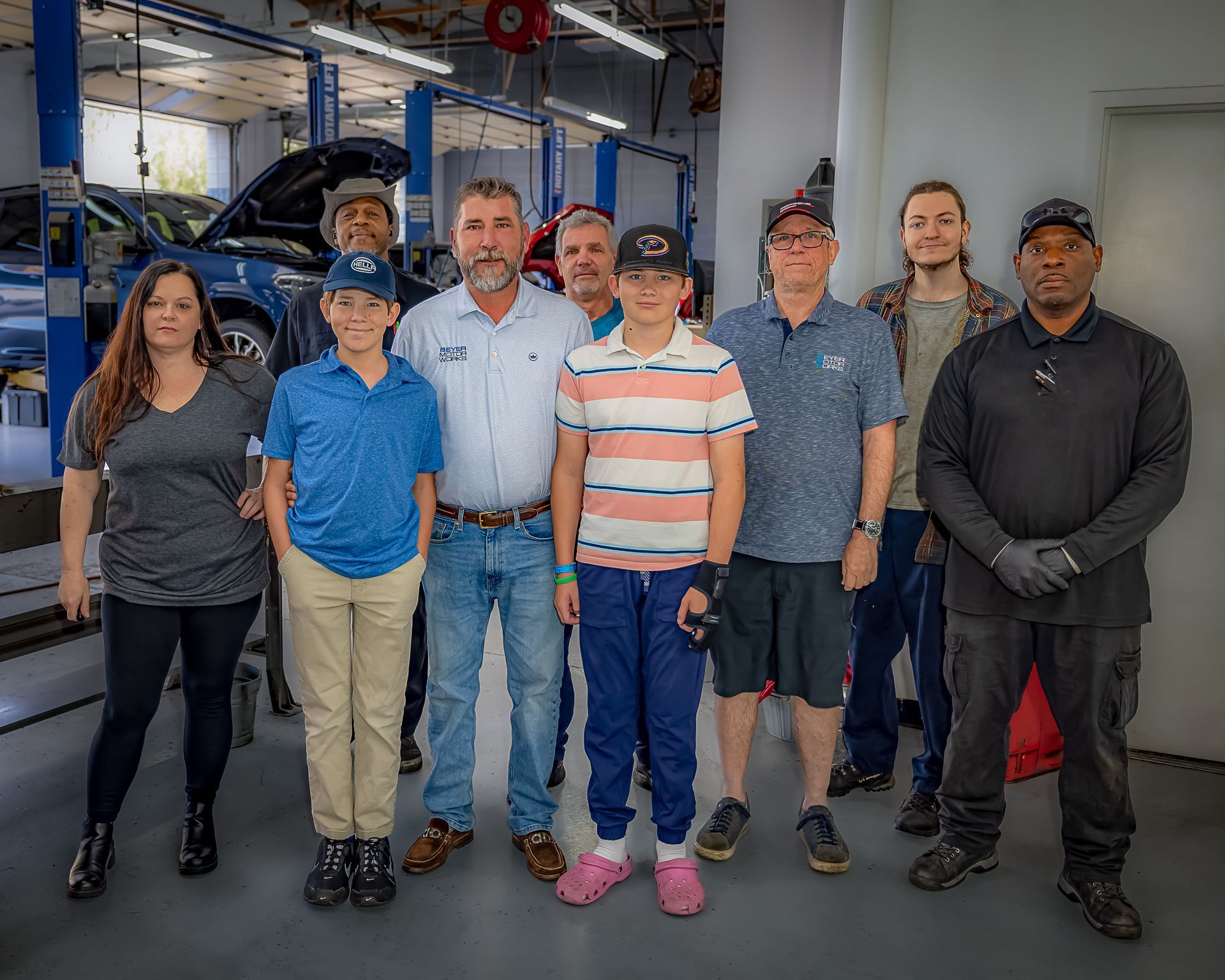 Group of people in a car repair shop. They are smiling, possibly posing.