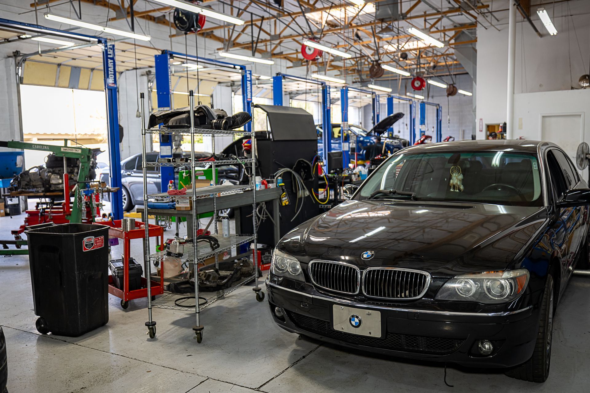 A black BMW car in a busy auto repair shop with multiple lifts and equipment.