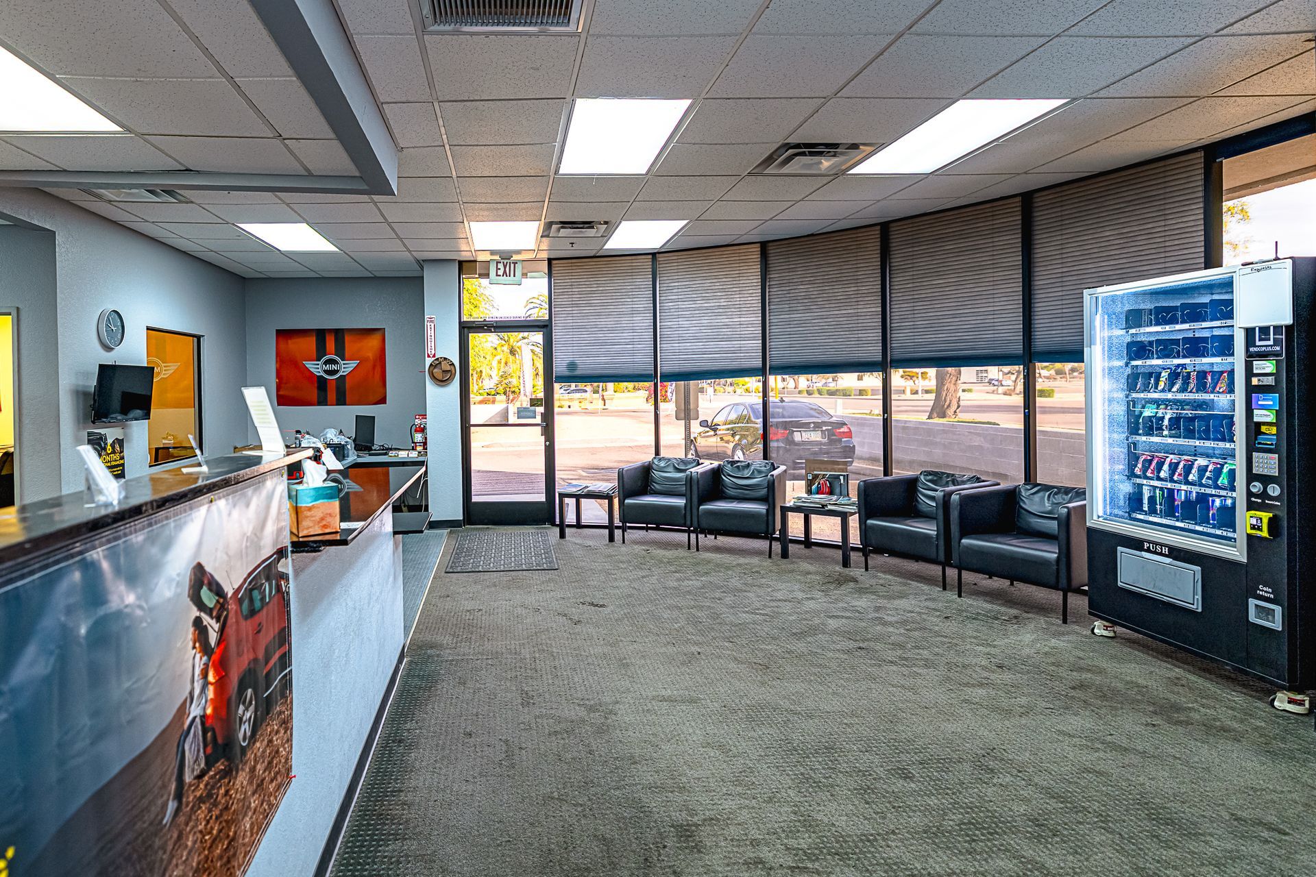 Reception area with waiting chairs, vending machine, front desk, and large windows.
