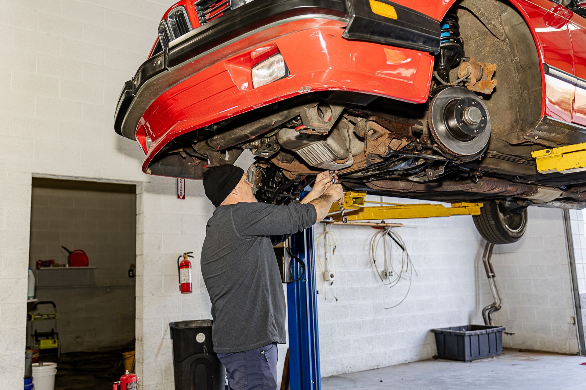 Mechanic working on a red car lifted on a hoist in a garage.