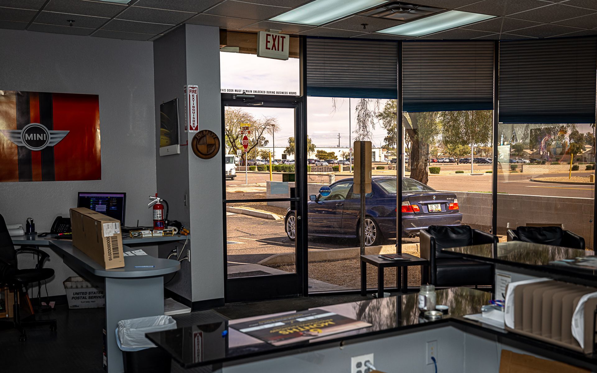 Interior auto shop: Mini logo on wall, counter, glass door to street with parked car.
