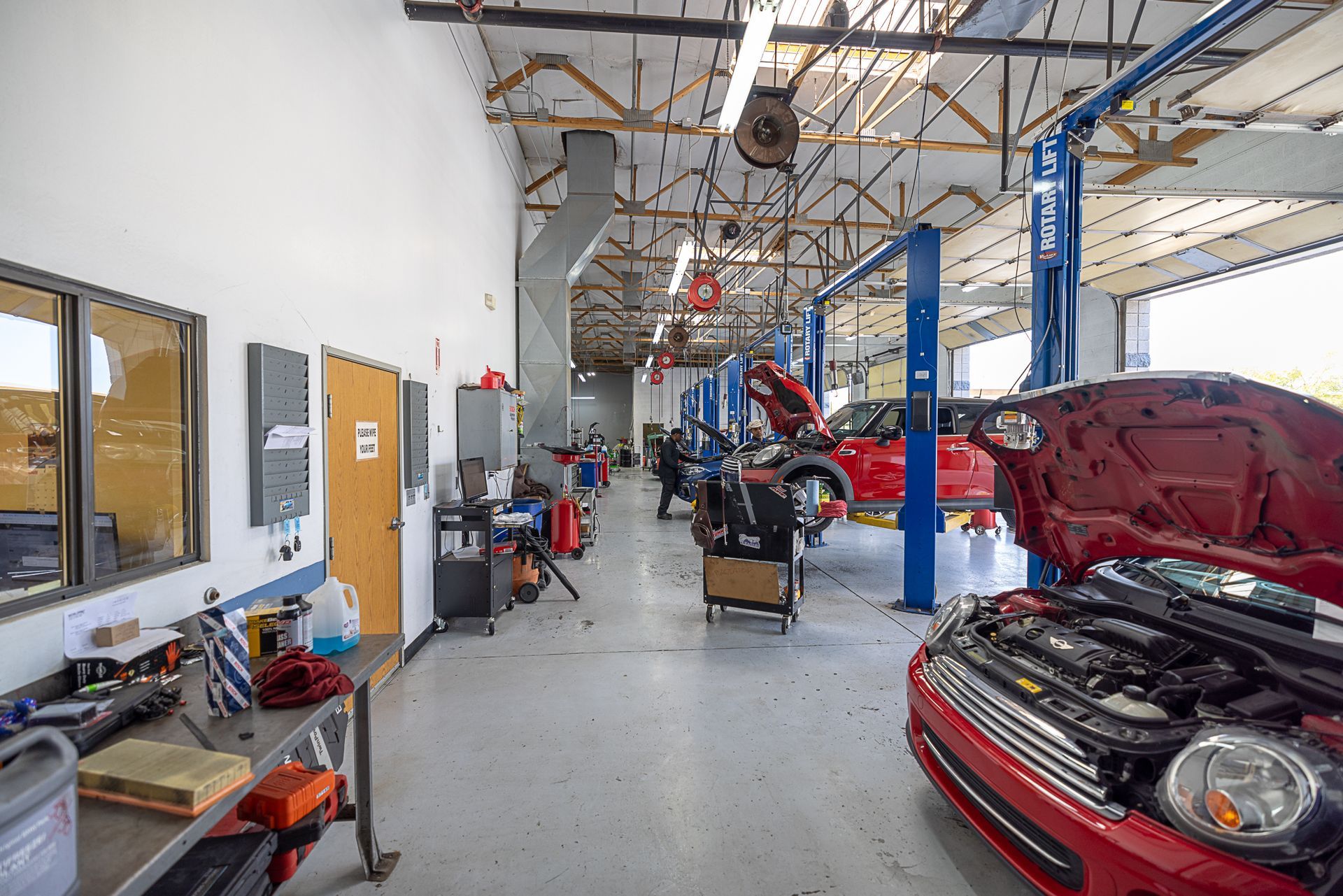 Interior of auto repair shop with cars on lifts, tools, and a technician.
